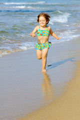 Happy toddler girl running on the beach