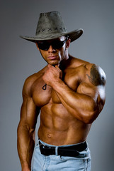 Muscular male in a hat and sunglasses on a gray background