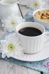 Breakfast with black coffee, apple tart, milk and white flowers