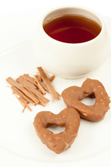 Two cookies in shape of heart, cup with tea and cinnamon sticks