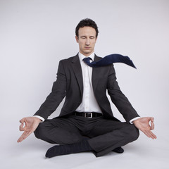 young businessman meditating in yoga lotus pose on white backgro