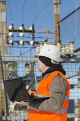 Electrician with computer near the electricity substation