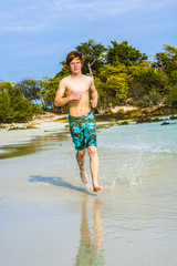 young boy with red hair jogging along the tropical beach