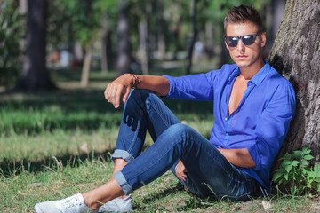 Fototapeta premium serious man sits on ground next to tree