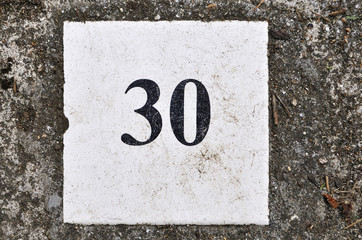 white tile with the number 30 on a texture background concrete