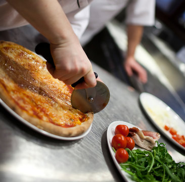The hand close up of the baker of the cook cuts a pizza on kitch