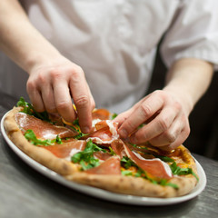 Closeup hand of chef baker in white uniform making pizza at kitc