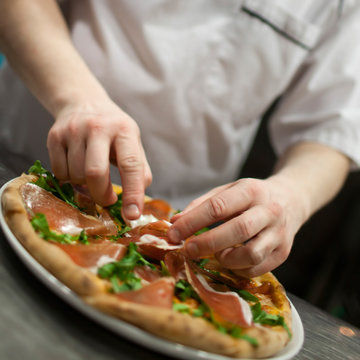 Closeup hand of chef baker in white uniform making pizza at kitc