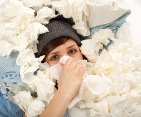 Das junge M&auml;dchen liegt krank im Bett und putzt sich die Nase