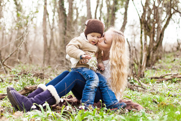 Smiling mother and little son on grass and snowdrops