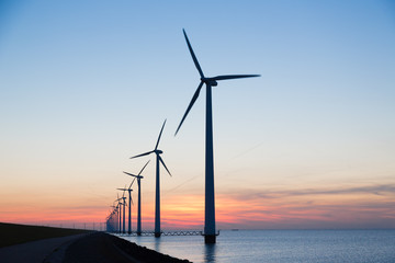 Long row of windturbines with sunset over the sea