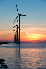 Long row of windturbines with sunset over the sea