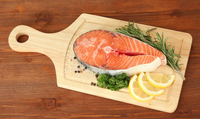Fresh salmon steak on cutting board, on wooden background
