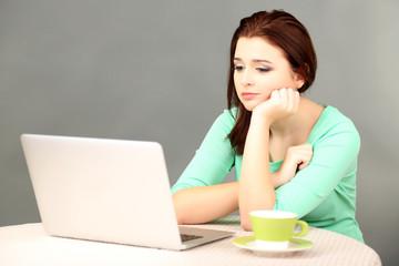 Fototapeta premium Beautiful young woman working on laptop on grey background
