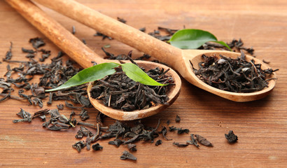 Dry tea with green leaves in wooden spoons, on wooden