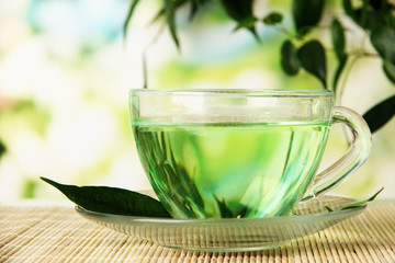 Transparent cup of green tea on bamboo mat, on nature