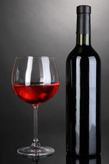 Red wine glass and bottle of wine on grey background