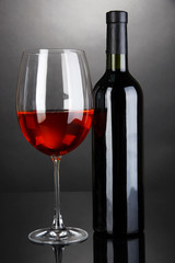 Red wine glass and bottle of wine on grey background
