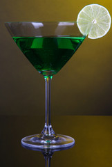 Green cocktail in martini glass on dark yellow background