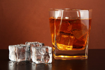 Glass of whiskey and ice on brown background
