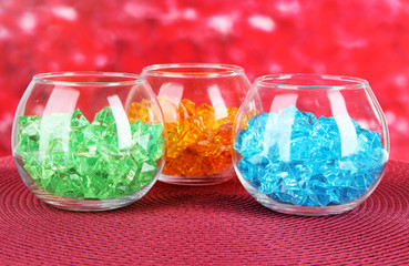 Glasses with colorful decorative stones on bright background