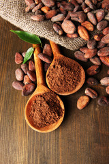 Cocoa powder in spoons and cocoa beans on wooden background