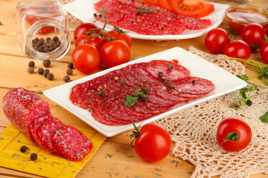 Tasty salami on plates on wooden table close-up