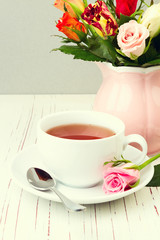 Cup of tea on wooden table with rose flowers
