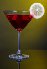 Red cocktail in martini glass on dark yellow background
