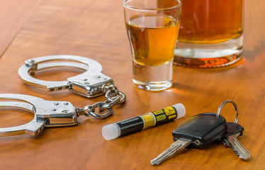 Schnapsglas mit Autoschlüssel, Alkoholtester und Handschellen