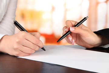 Two business partners signing document, on bright background