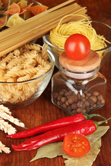 Different types of pasta, spices, tomatoes on a wooden table
