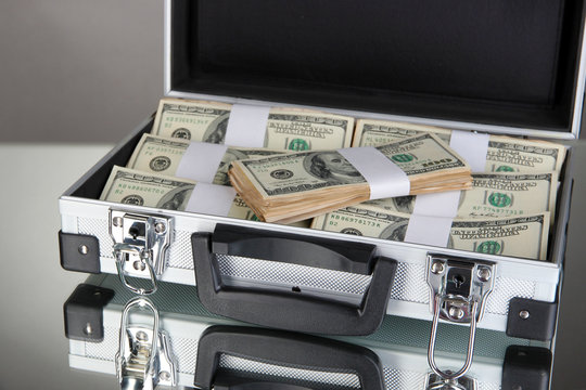 Suitcase with 100 dollar bills on grey background