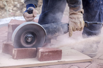 worker uses a stone cutter to cut the brick pavers