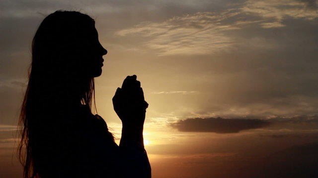 Prayer. Woman with hands folded at seaside during sunset.