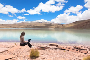 Young girl with a laptop on the shore of a mountain lake