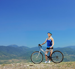 Young female biker posing with a mountain bike outdoors