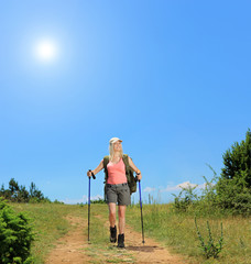Young woman with backpack and hiking poles walking at sunny day
