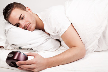 beautiful young man lying in bed looking at clock