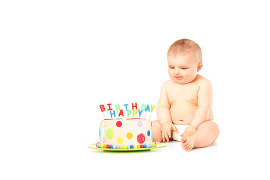 A 9 month old baby in diapers sitting next to a birthday cake