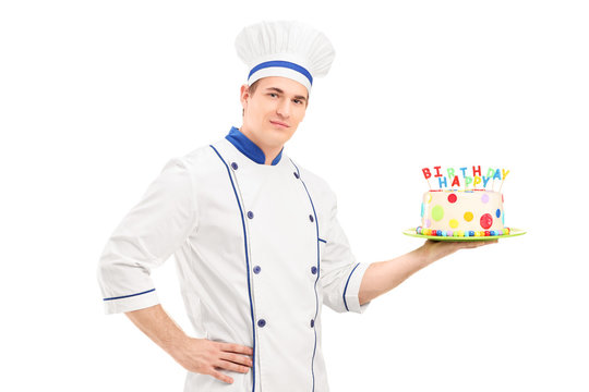 Young male chef in a uniform holding a decorated birthday cake