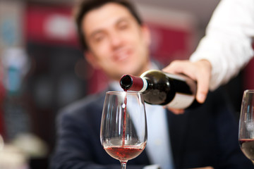 Waiter pouring red wine to a man