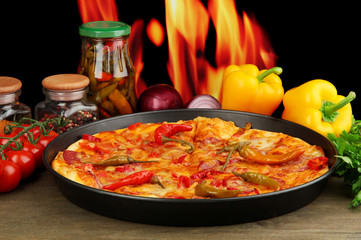 Tasty pepperoni pizza in pan with vegetables on flame