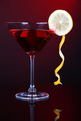 Red cocktail in martini glass on dark red background