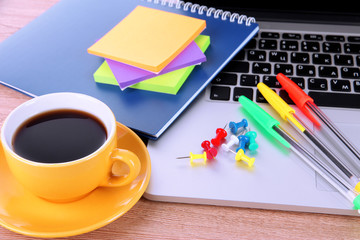 Laptop with stationery and cup of coffee on table