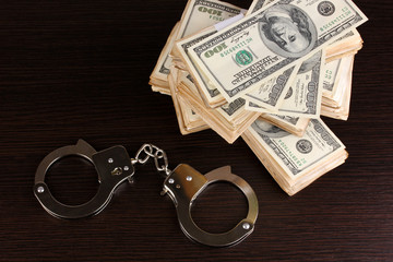 Handcuffs and packs of dollars on wooden table close-up