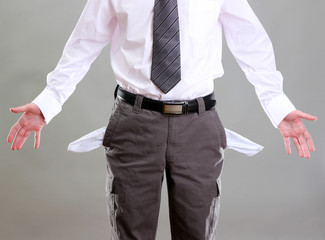 Business man showing his empty pockets, on grey background