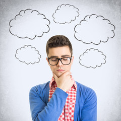 Young nerdy geek wearing glasses with cloud thought bubbles