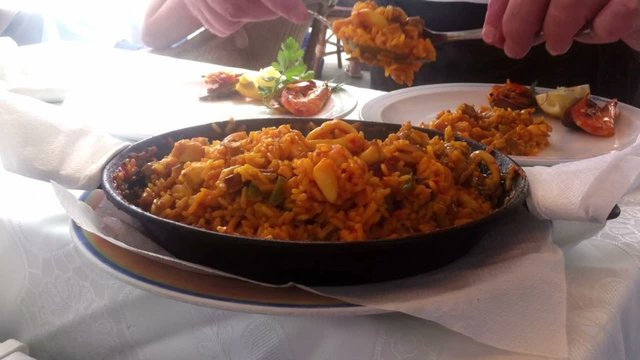 Waiter serving seafood paella in the pan, typical Spanish dish (