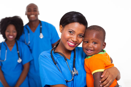 black pediatrician and baby boy with co-workers on background